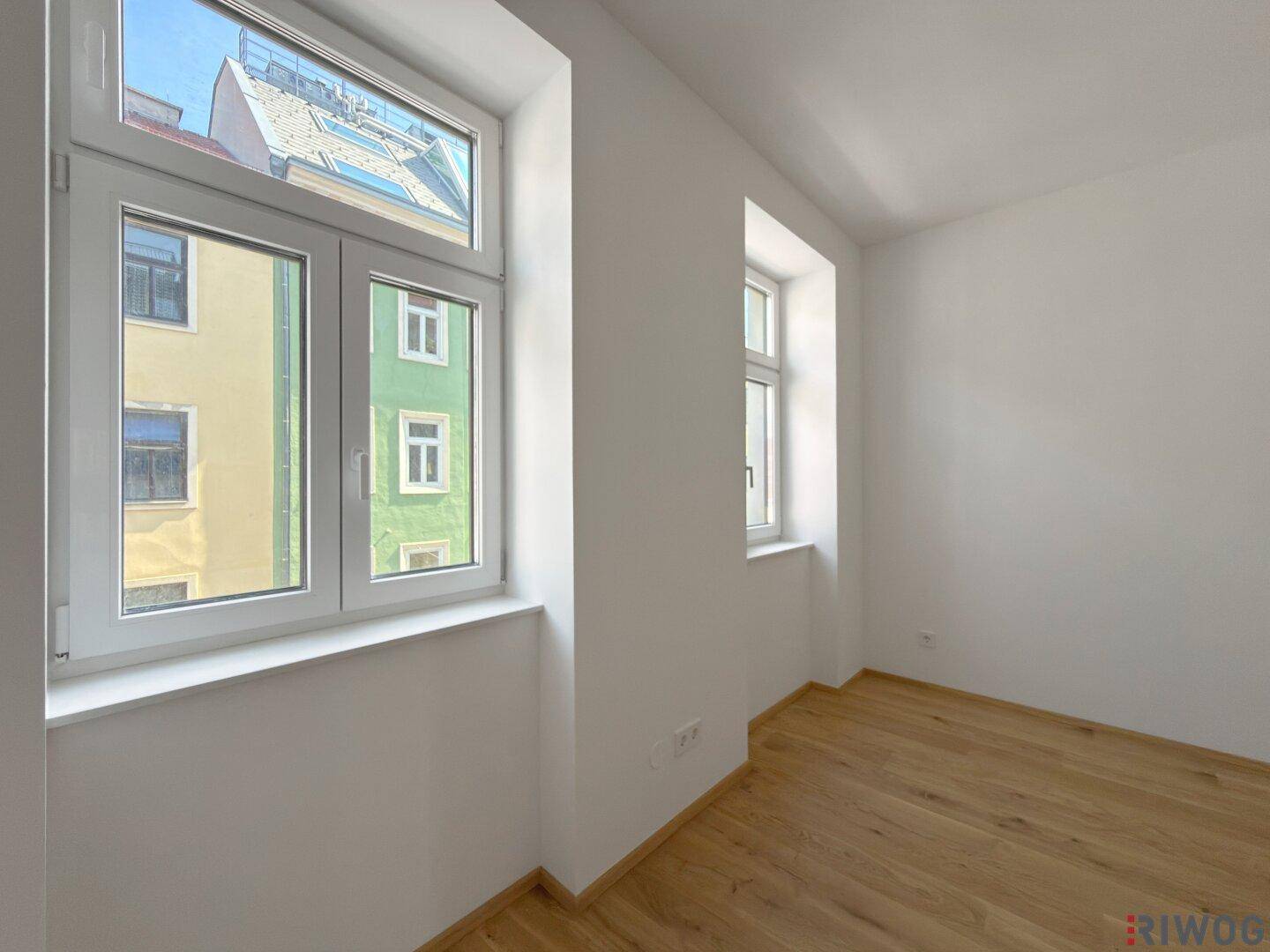 Schlafzimmer mit Parkettboden und Blick aus dem Fenster auf die Nachbargebäude.