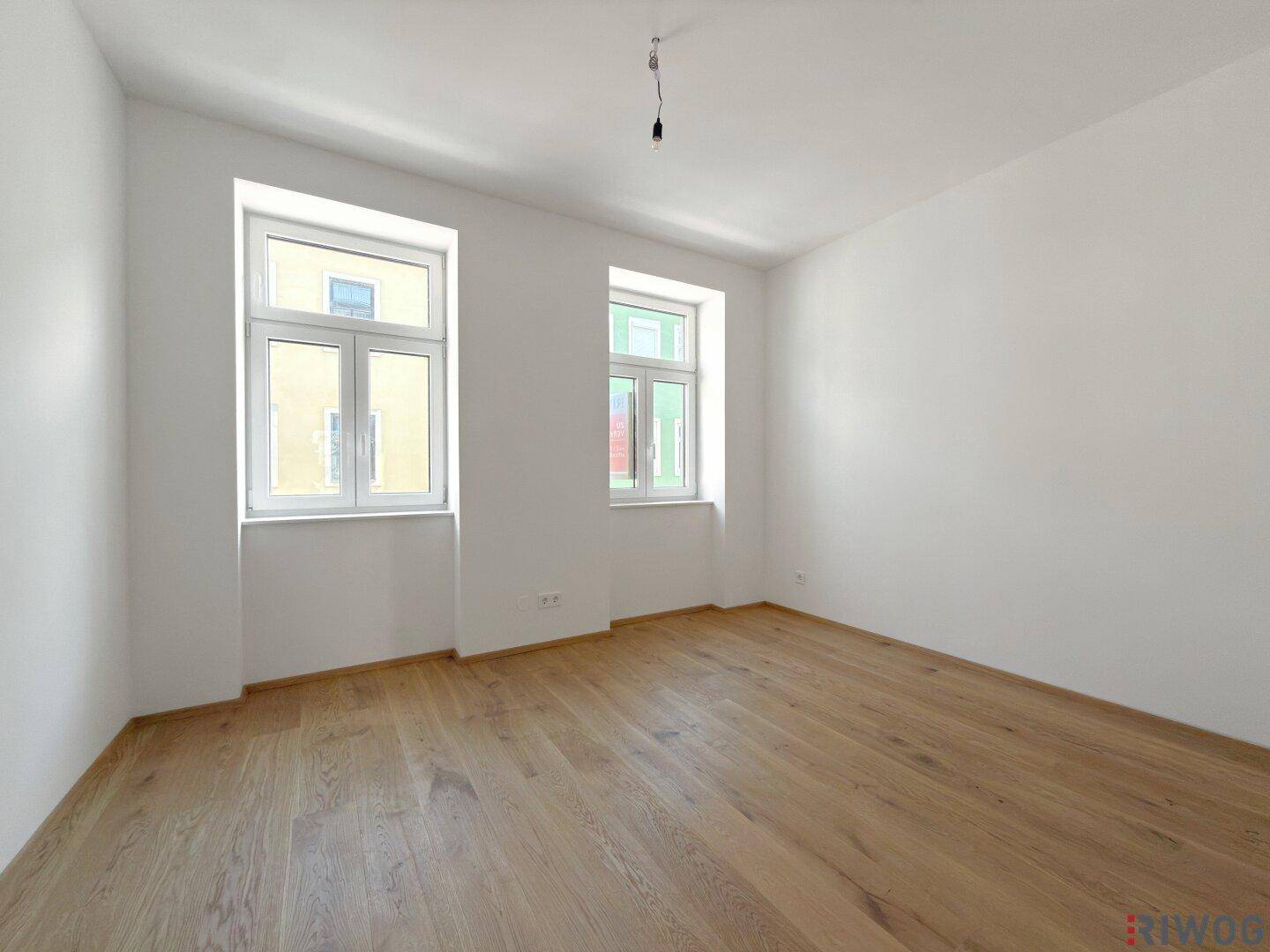 Helles Schlafzimmer mit zwei Fenstern und neu verlegtem Parkettboden.