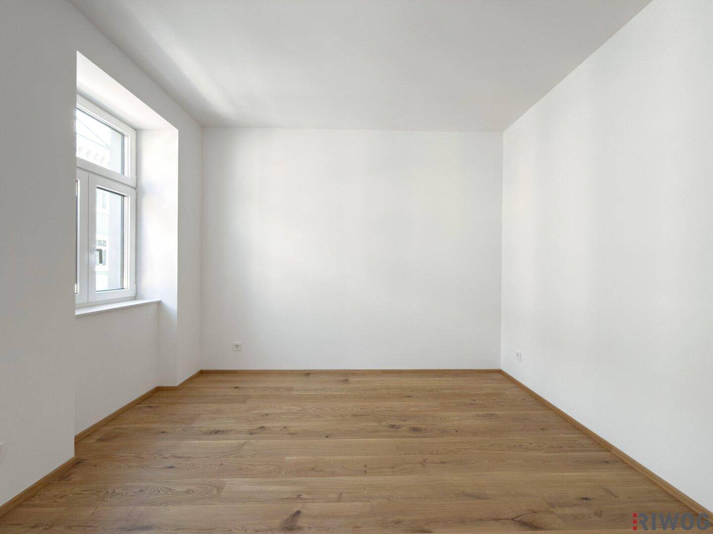 Ruhiges Schlafzimmer mit hellem Parkettboden und einem großen Fenster.