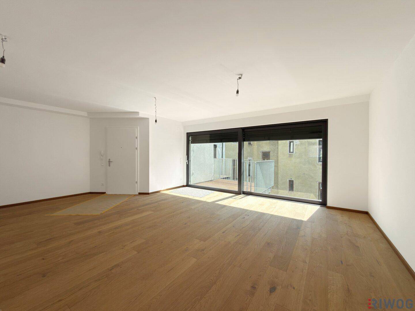 Lichtdurchfluteter Wohnraum mit Holzboden, weißen Wänden und Zugang zu einem Balkon.