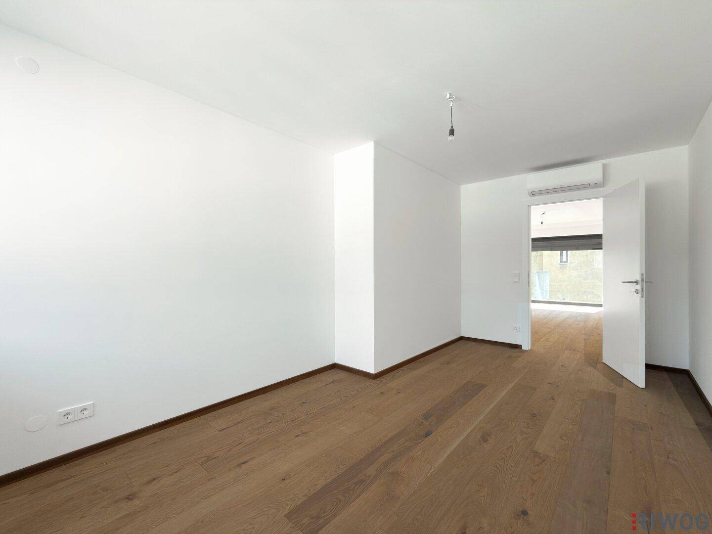 Helles Zimmer mit Holzboden, weißen Wänden und einer Klimaanlage über dem Türrahmen.