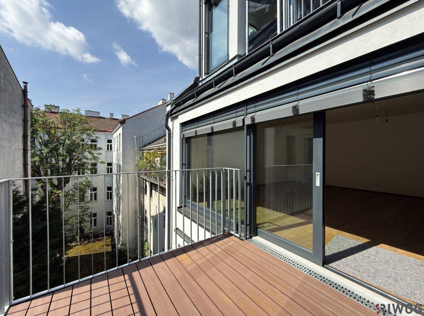 Geräumiger Balkon mit Holzboden und Blick auf den Innenhof, zugänglich durch große Schiebetüren.