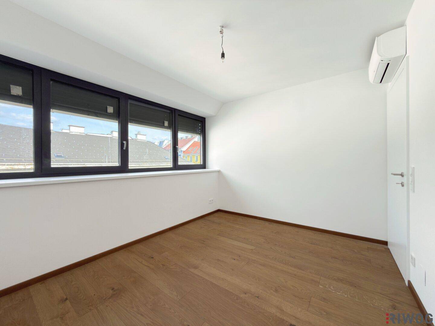 Geräumiges Schlafzimmer mit Holzboden, mehreren Fenstern und integrierter Klimaanlage.