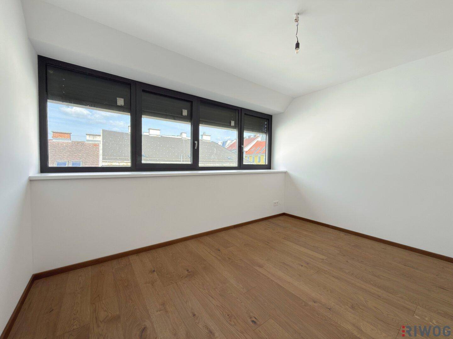 Geräumiges Schlafzimmer mit Holzboden, mehreren Fenstern und integrierten Rollläden.