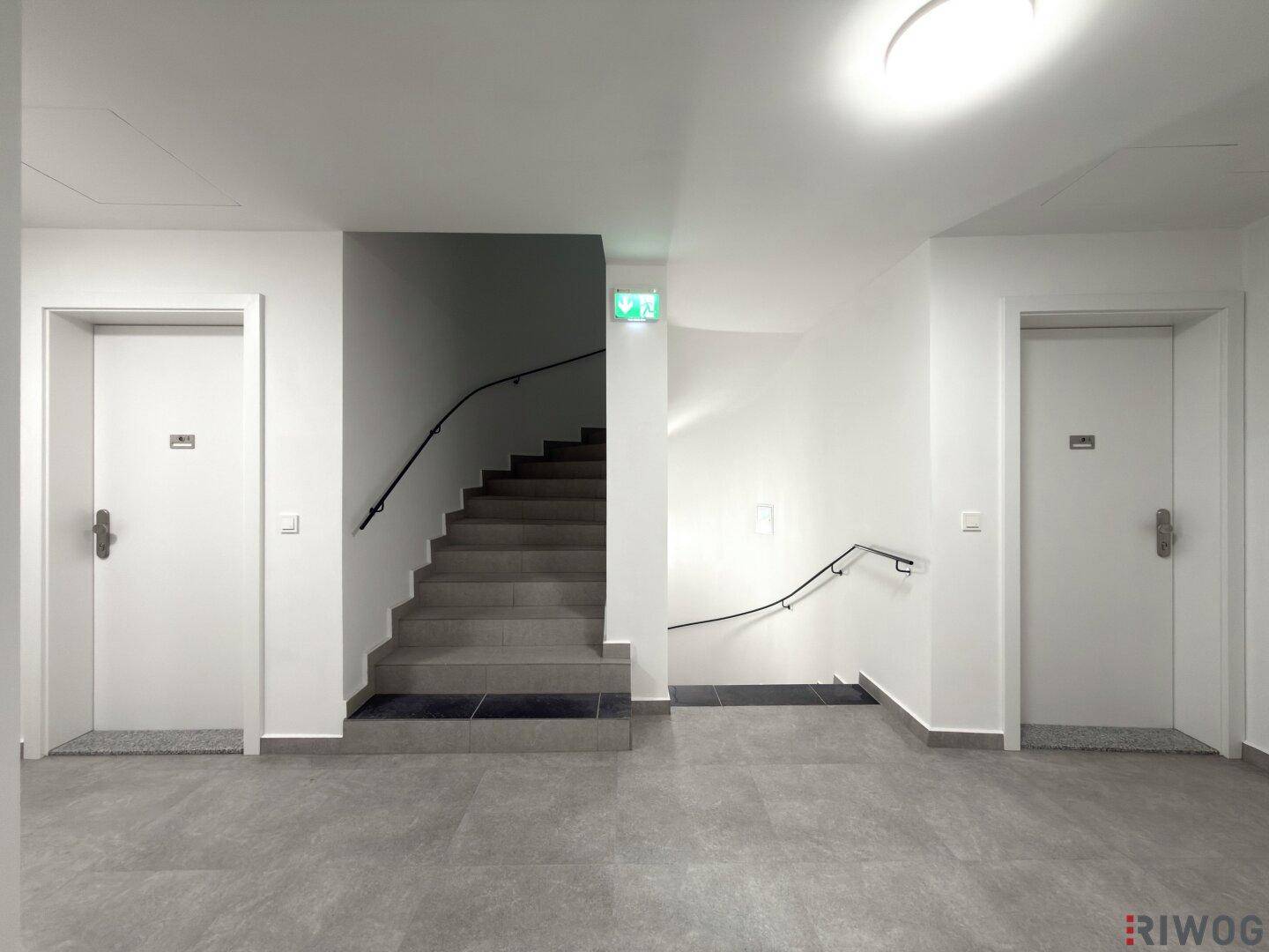 Heller Flur mit Treppenhaus, mehreren Türen und Fliesenboden im Gemeinschaftsbereich.