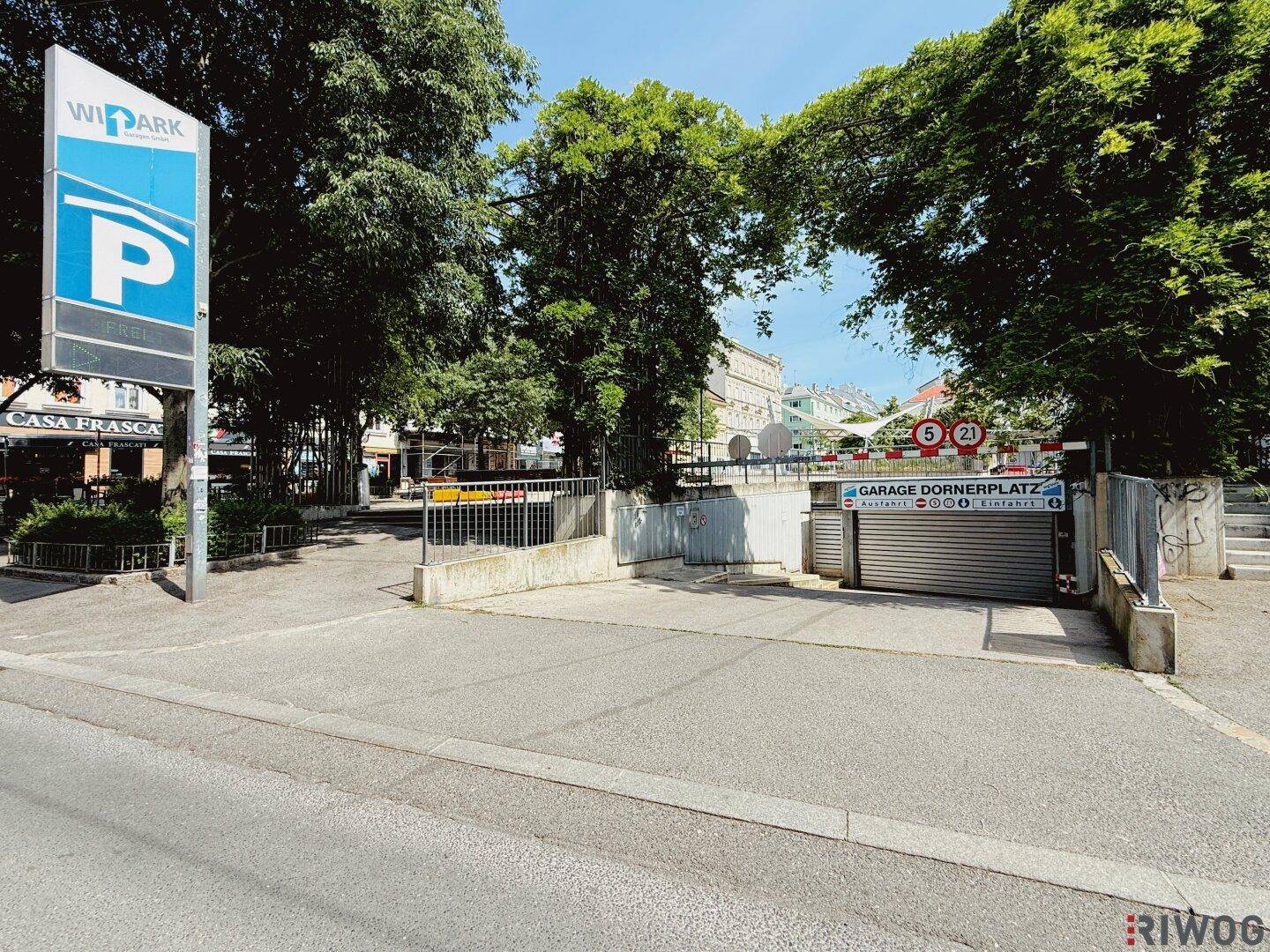 Einfahrt zu einer Tiefgarage mit WIPARK-Beschilderung und umliegenden Bäumen.