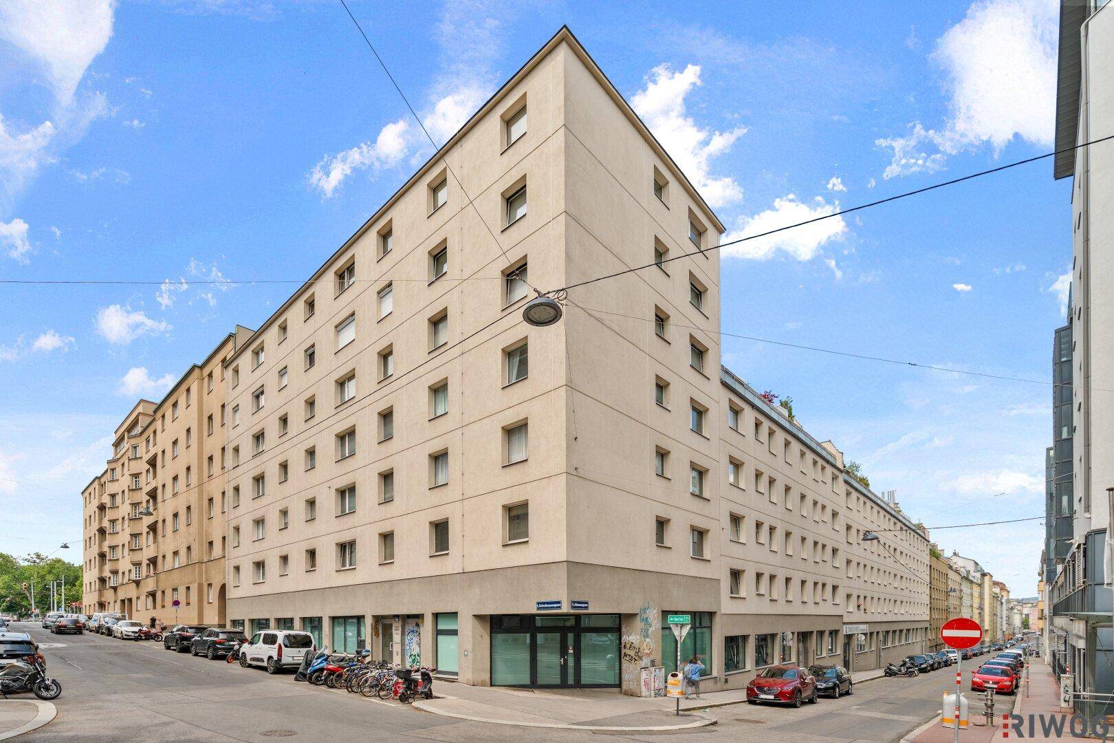 Modernes Eckgebäude in der Stadt mit vielen Fenstern und einer belebten Straße davor.
