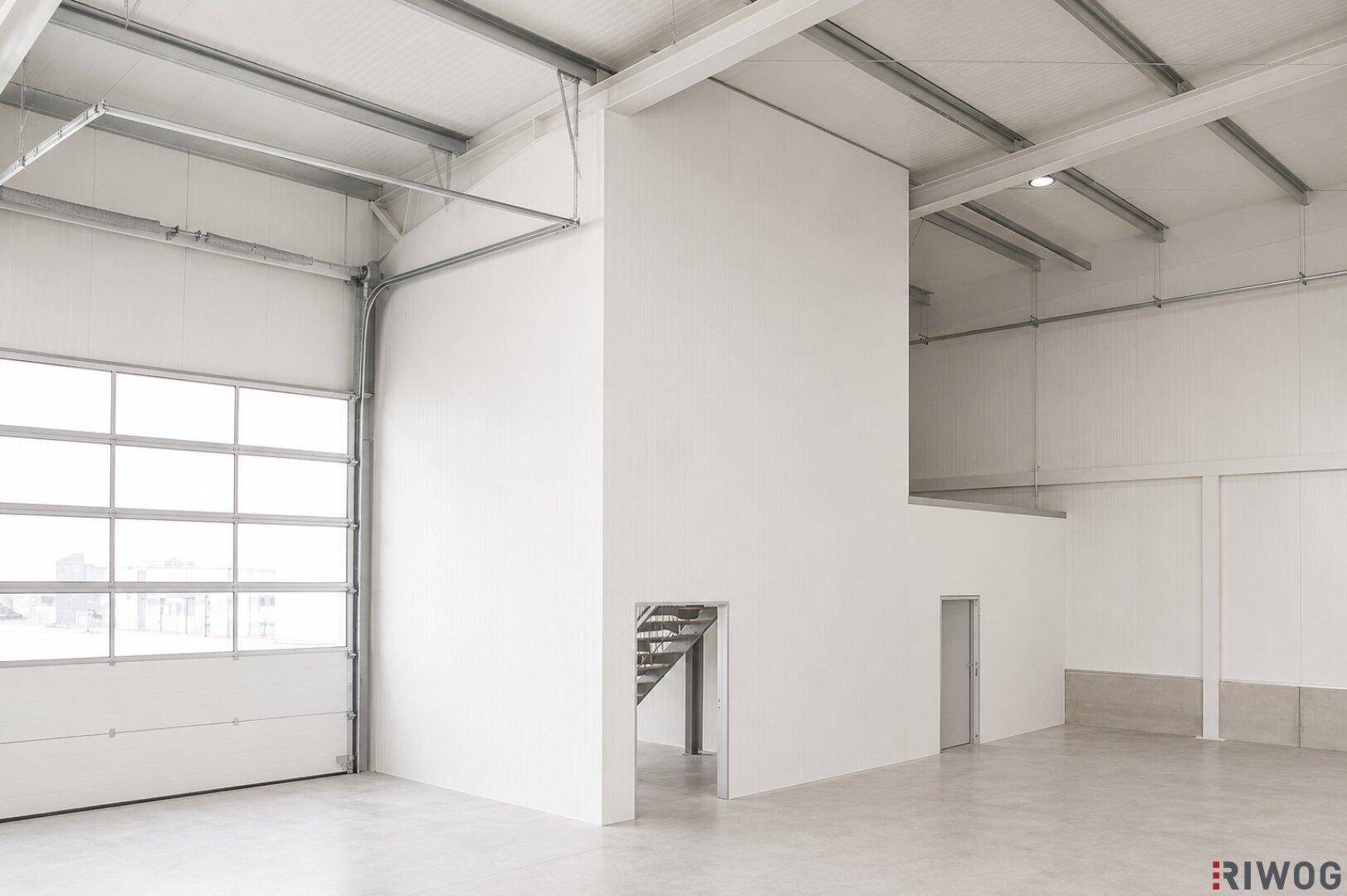 Geräumige Lagerhalle mit hohen Decken, Betonboden und einem großen Rolltor für den Zugang.