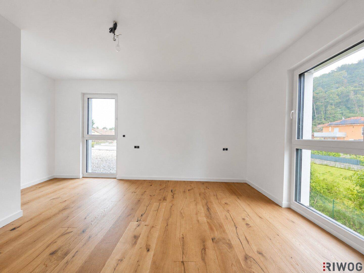 Helles Schlafzimmer mit Holzboden und großen Fenstern, die viel Tageslicht hereinlassen und Blick ins Grüne bieten.