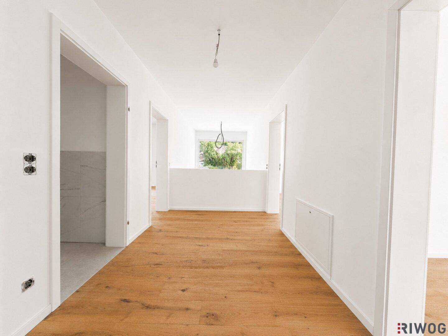Heller Flur mit Holzboden und Zugang zu verschiedenen Räumen im Haus, mit Fenster am Ende.