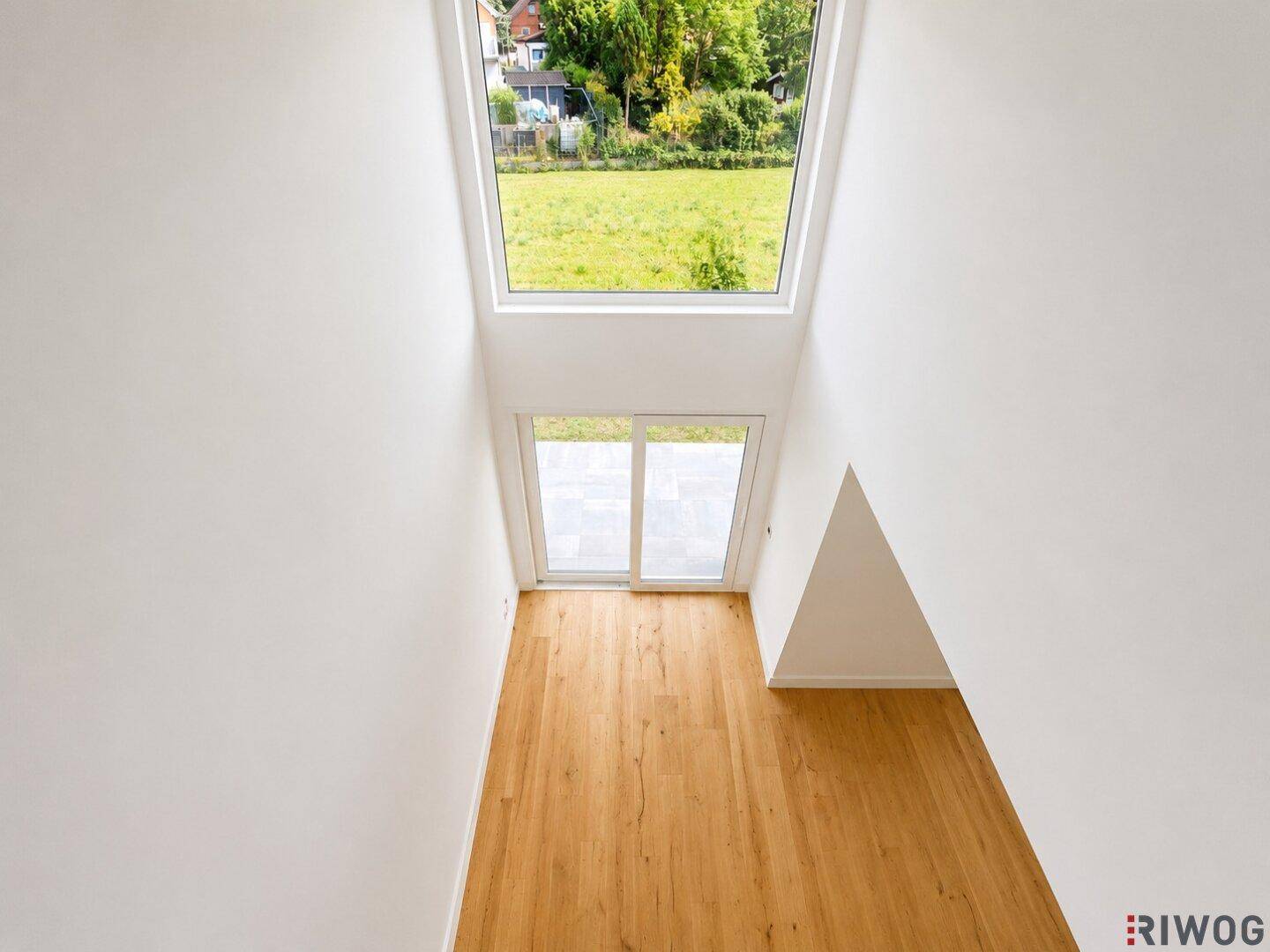 Blick von der oberen Etage in den unteren Bereich mit großen Fenstern und Holzboden, sehr hell.