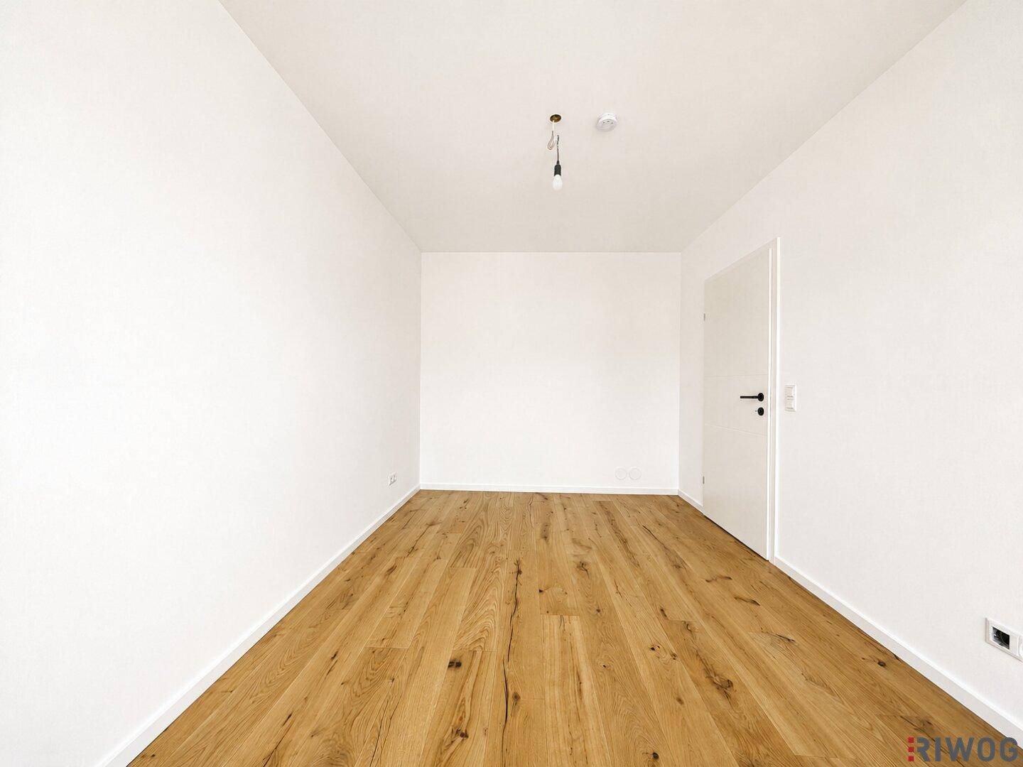 Leeres Zimmer mit Holzboden und weiß gestrichenen Wänden, bereit für die individuelle Gestaltung und Nutzung.