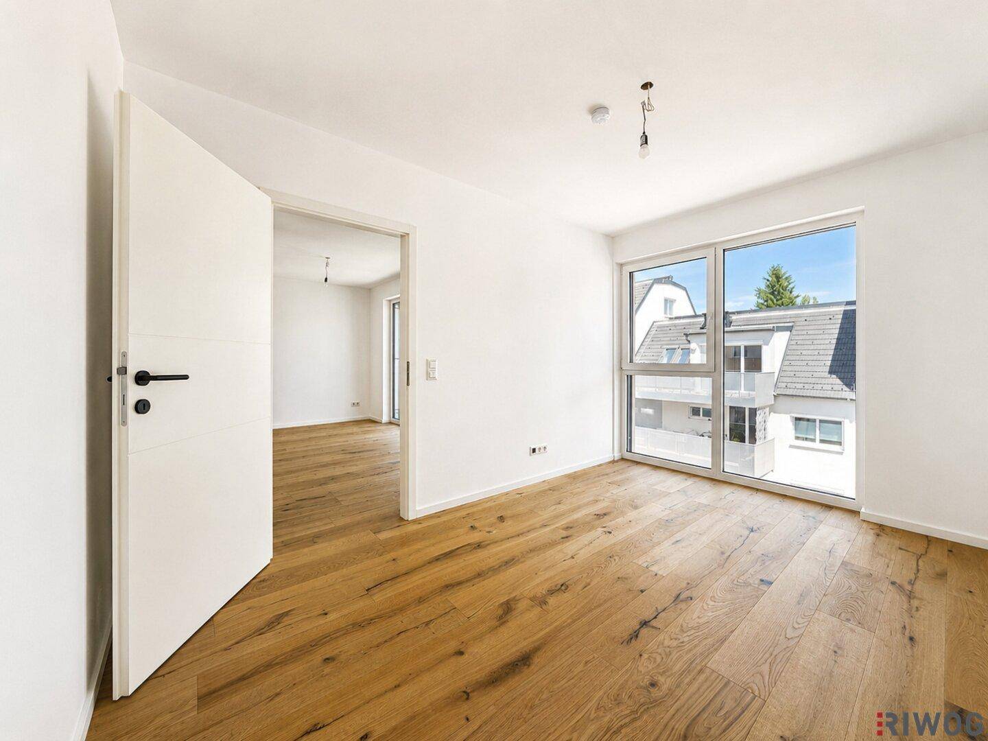Geräumiges Zimmer mit Holzboden und großen Fenstern, die einen hellen und freundlichen Raum schaffen.