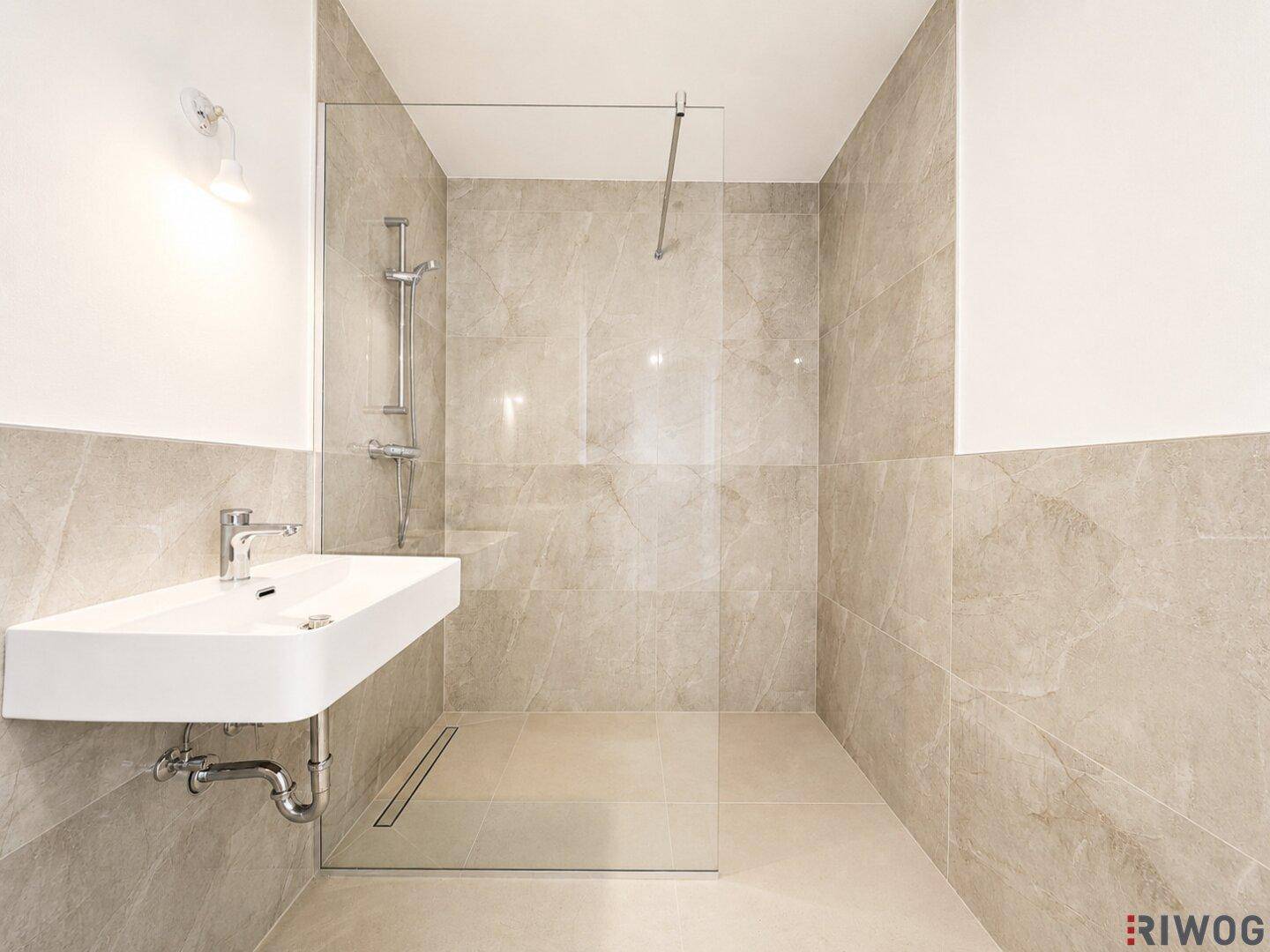 Stilvolles Badezimmer mit großer begehbarer Dusche und modernem Waschbecken, alles in hellen Grautönen gehalten.