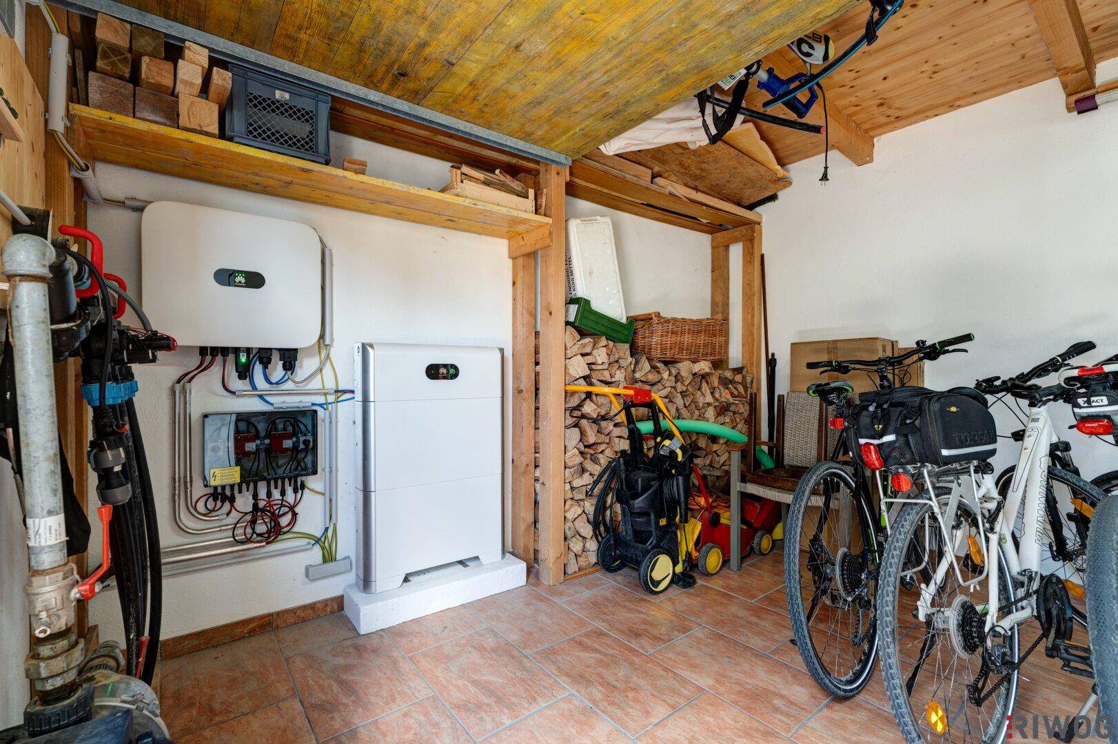 Praktischer Technikraum mit Solaranlage, Fahrrädern und Holzvorrat unter einer Holzdecke.