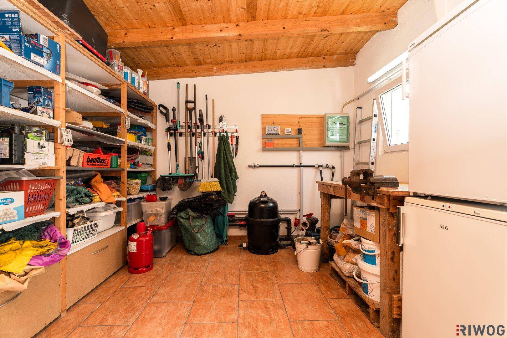Funktionaler Hauswirtschaftsraum mit Holzdecke, Regalen und Stauraum für Werkzeuge und Geräte.