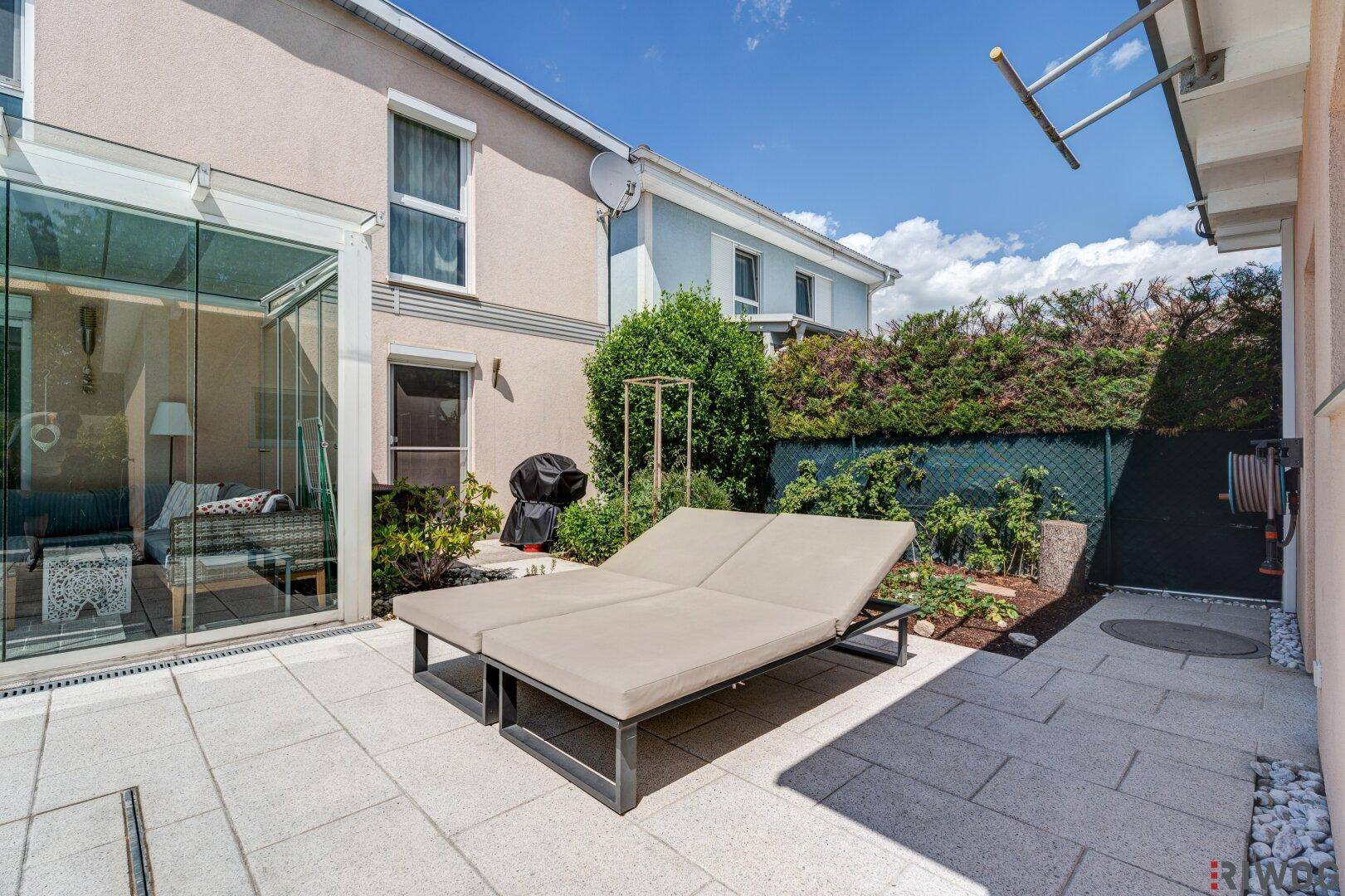Gemütliche Terrasse mit Sonnenliege und Grillbereich neben dem Glas-Wintergarten.