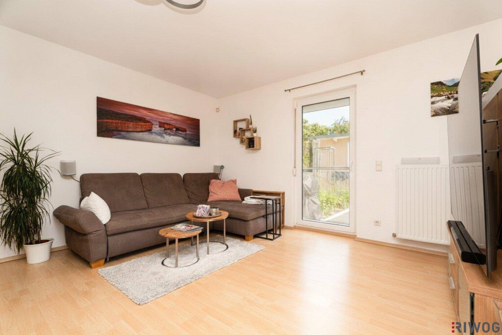 Modernes Wohnzimmer mit beigem Sofa, Holzboden und Zugang zum Außenbereich.