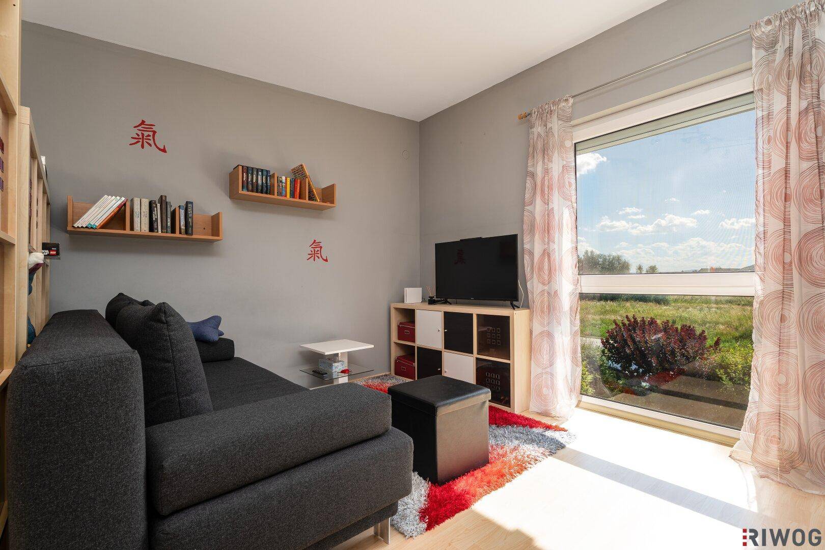 Helles Schlafzimmer mit grauem Sofa, Holzboden und weitem Blick ins Grüne.