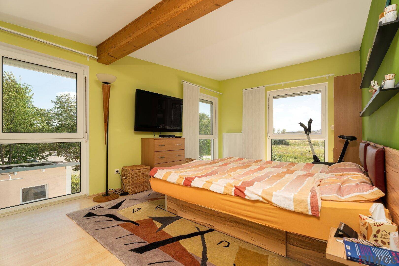 Geräumiges Schlafzimmer mit grünen Wänden, Holzbalken und großen Fenstern.