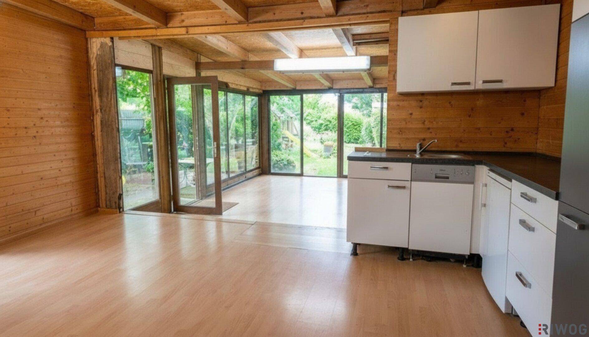 Kleine Küche mit weißen Schränken und Spülmaschine, integriert in einen hellen Raum mit Holzwänden und Gartenblick.