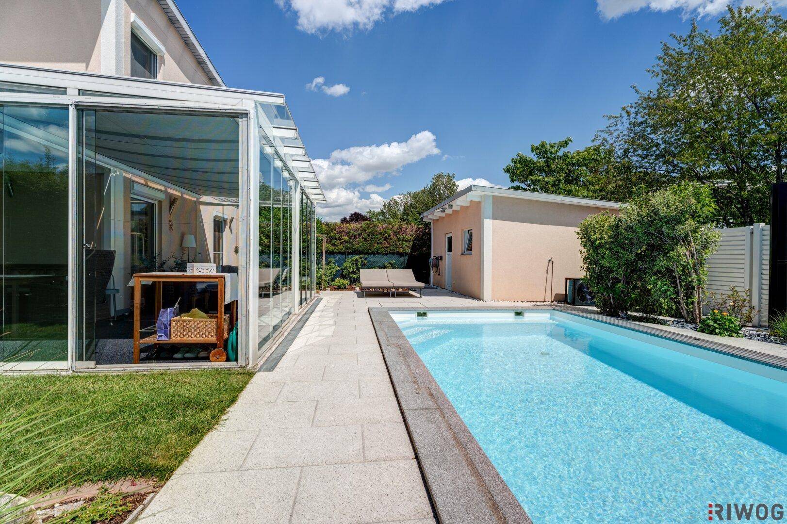Ansicht des Hauses mit Pool, Glas-Wintergarten und gepflegtem Gartenbereich.