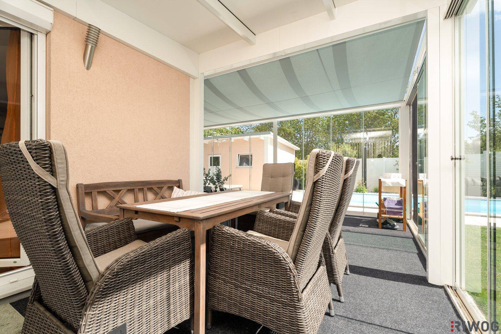 Heller Wintergarten mit Rattanmöbeln, Esstisch und Blick auf den Poolbereich.