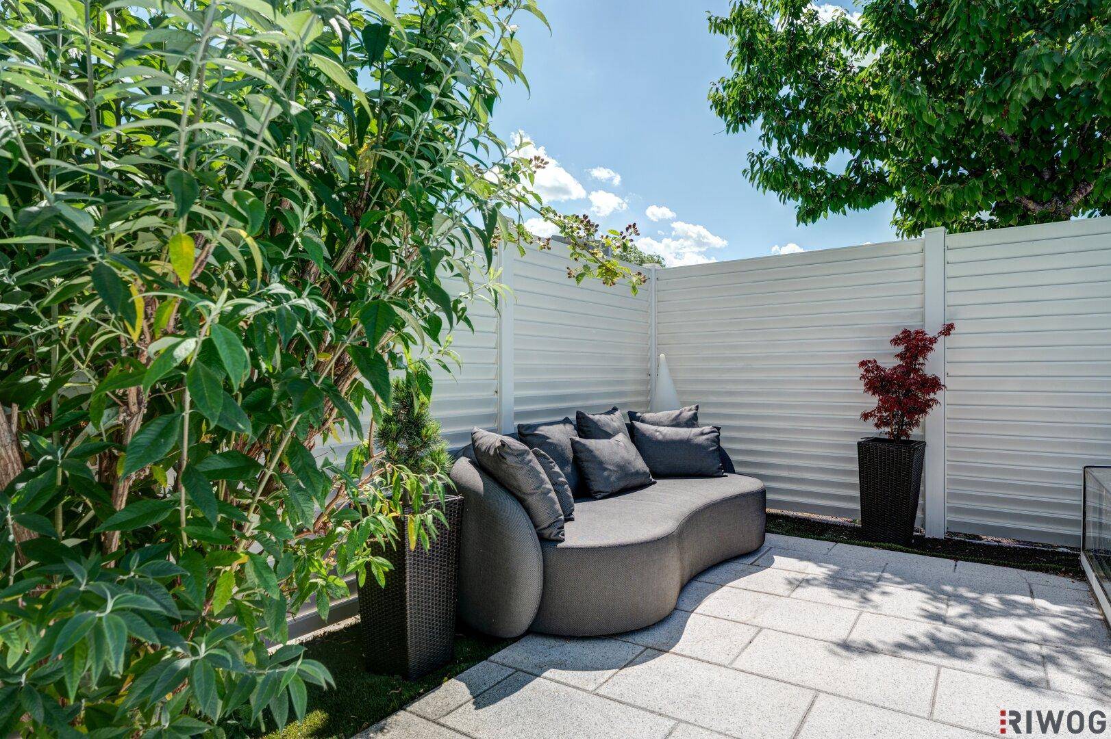Gemütliche Terrasse mit moderner Outdoor-Sitzgelegenheit und grüner Bepflanzung.