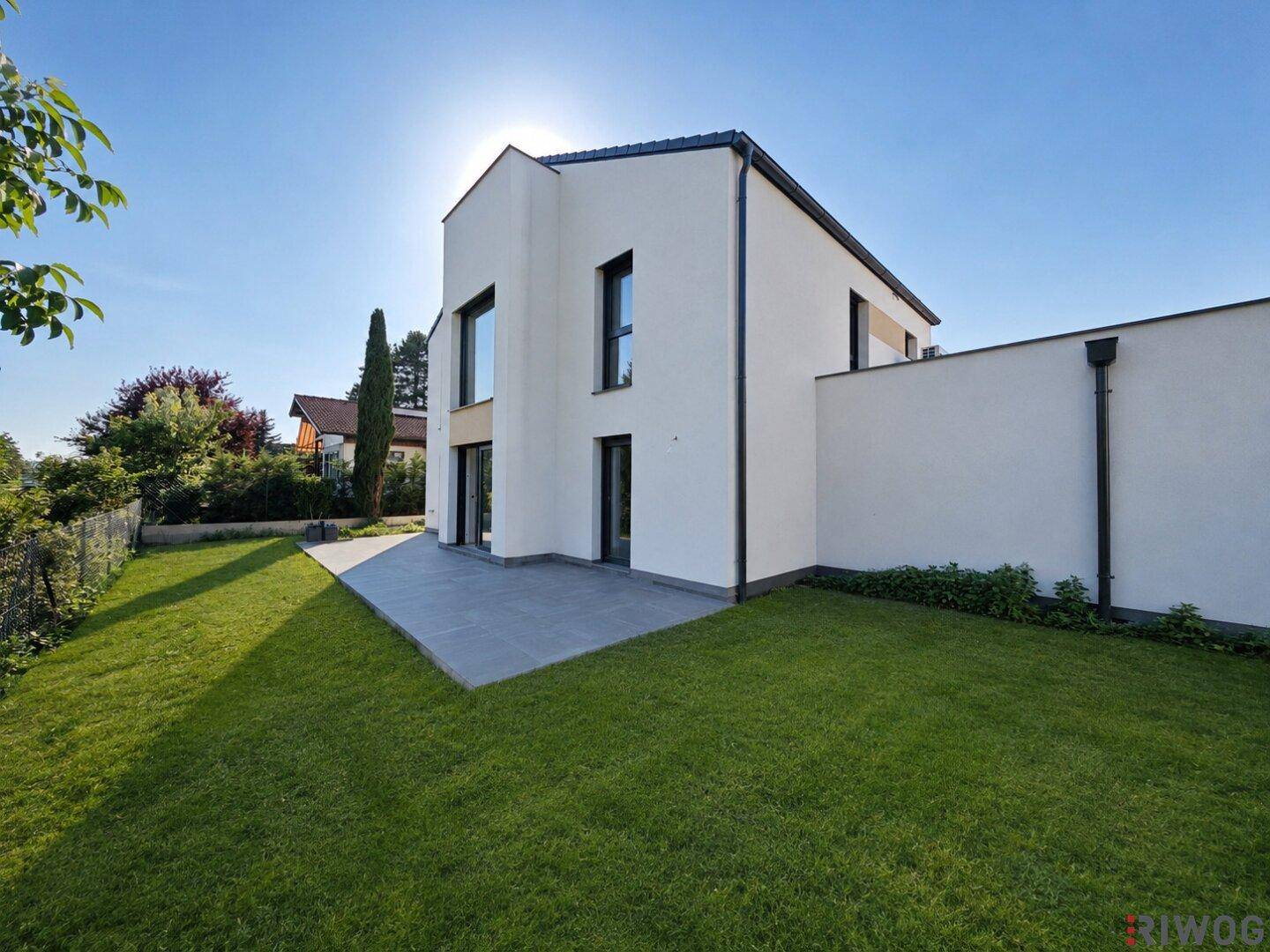 Sonnige Rückseite des Hauses mit großer Rasenfläche und einer modernen Terrasse.