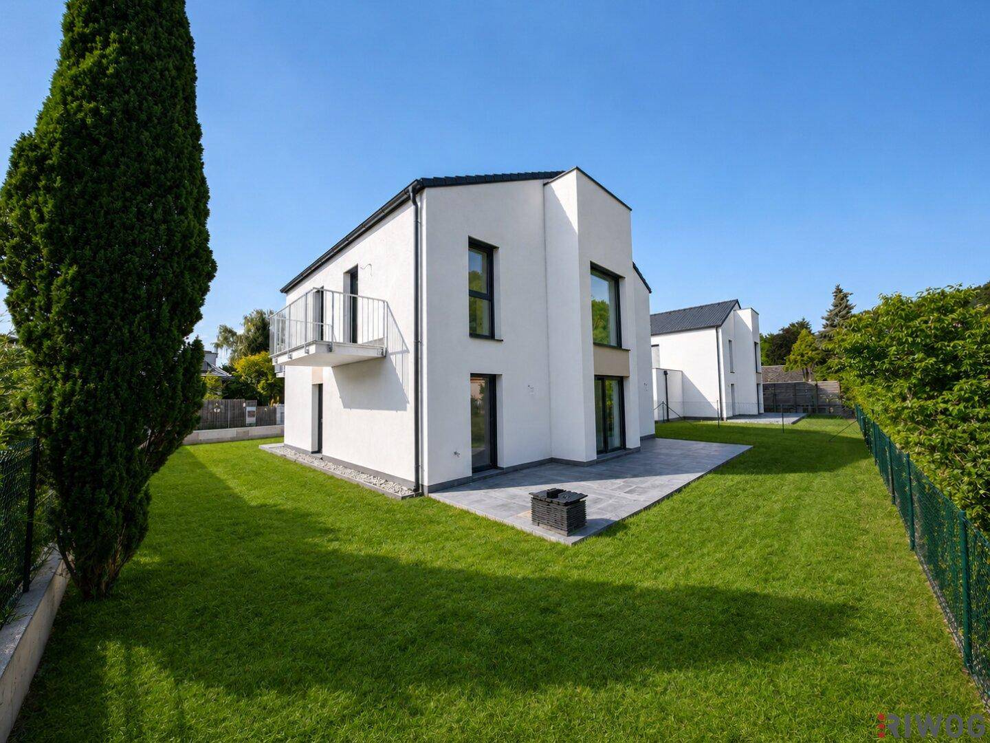 Seitenansicht des modernen Hauses mit gepflegtem Rasen, Terrasse und Balkon.