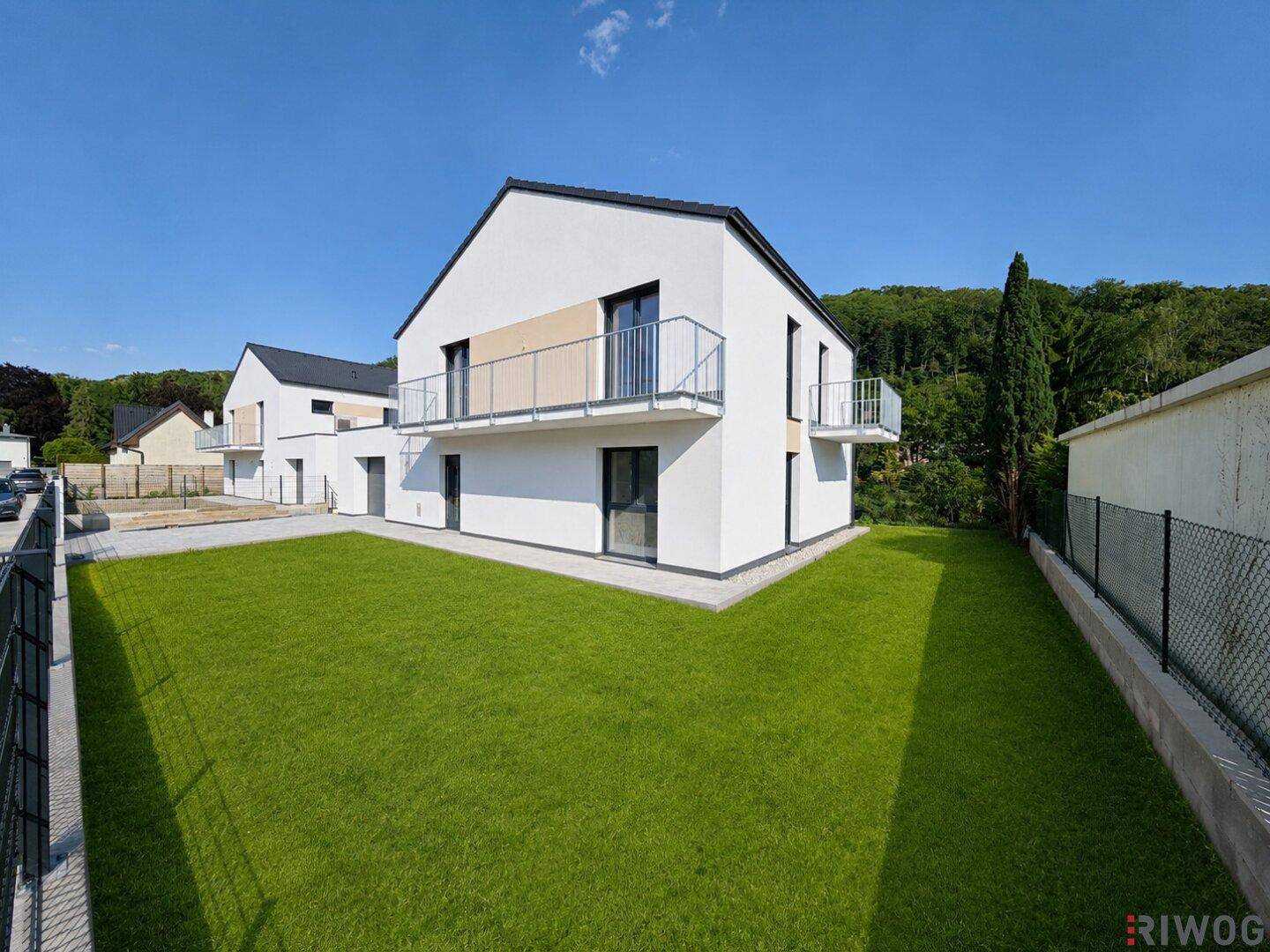 Rückansicht eines modernen Einfamilienhauses mit großem, gepflegtem Rasen und Balkonen.