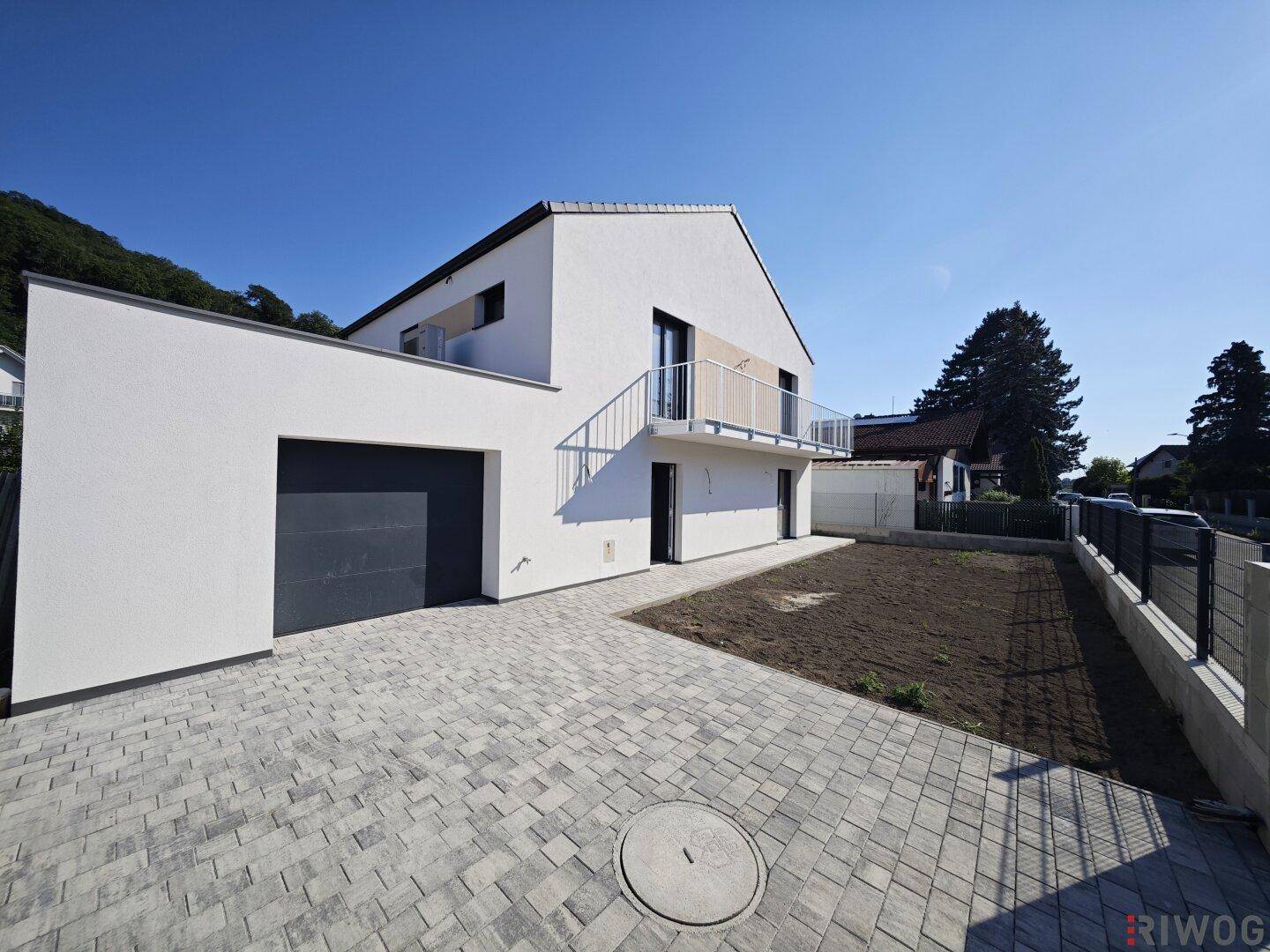 Modernes Einfamilienhaus mit weißer Fassade, integrierter Garage und gepflasterter Auffahrt unter blauem Himmel.