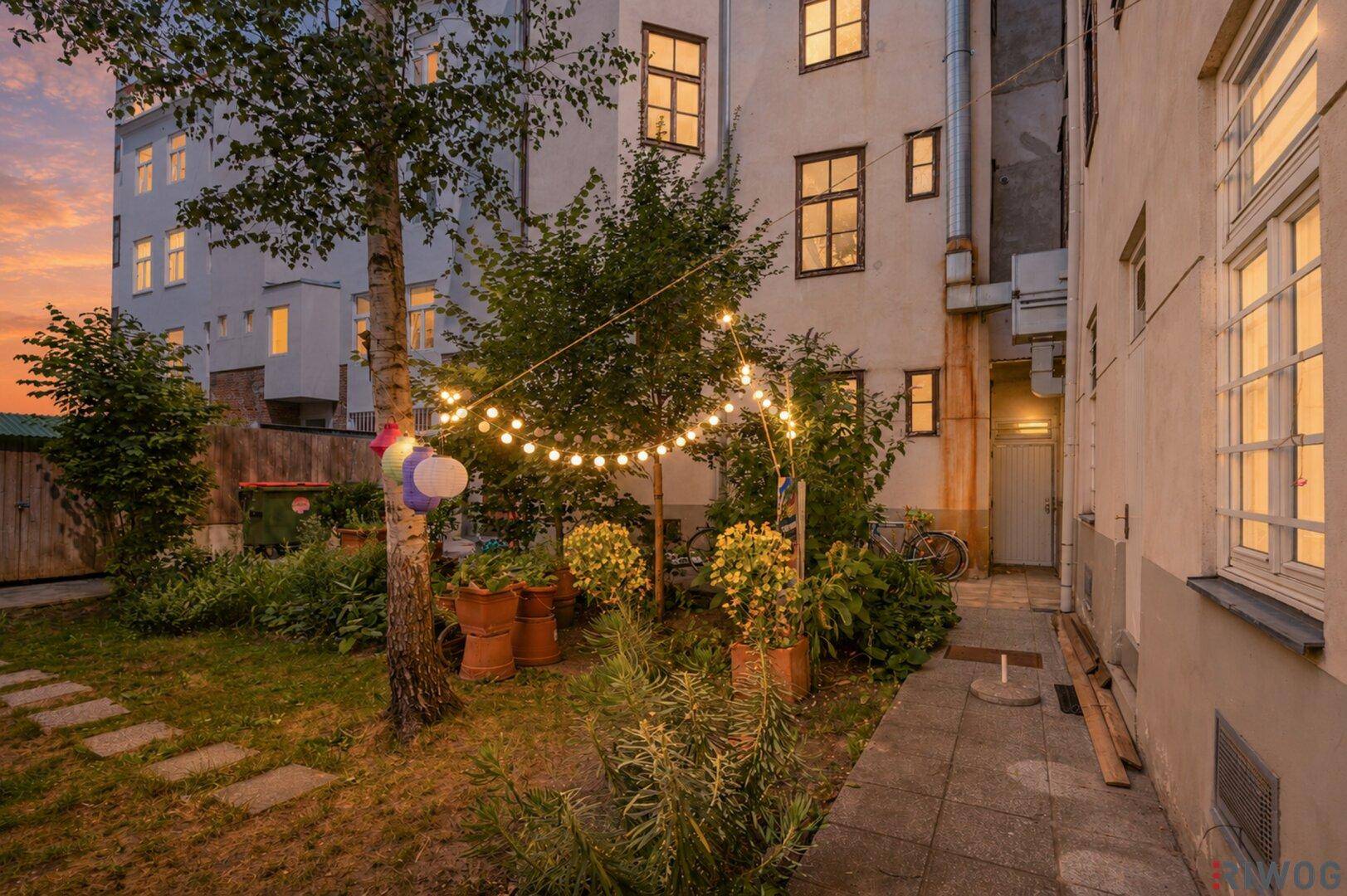 Gemütlicher Hinterhofgarten mit Lichterkette und Pflanzen bei Abenddämmerung, ideal zum Entspannen.