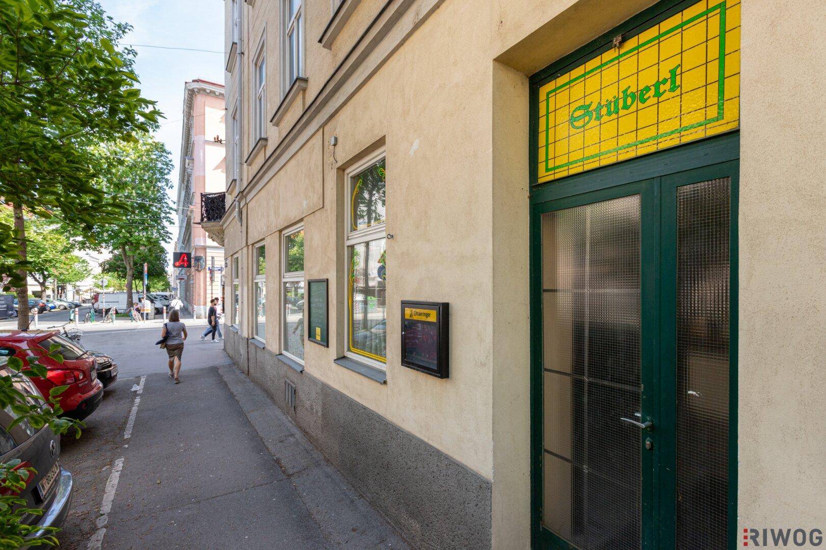 Nahaufnahme der Gebäudefassade mit grünem Eingang und Schaufenstern im Erdgeschoss.
