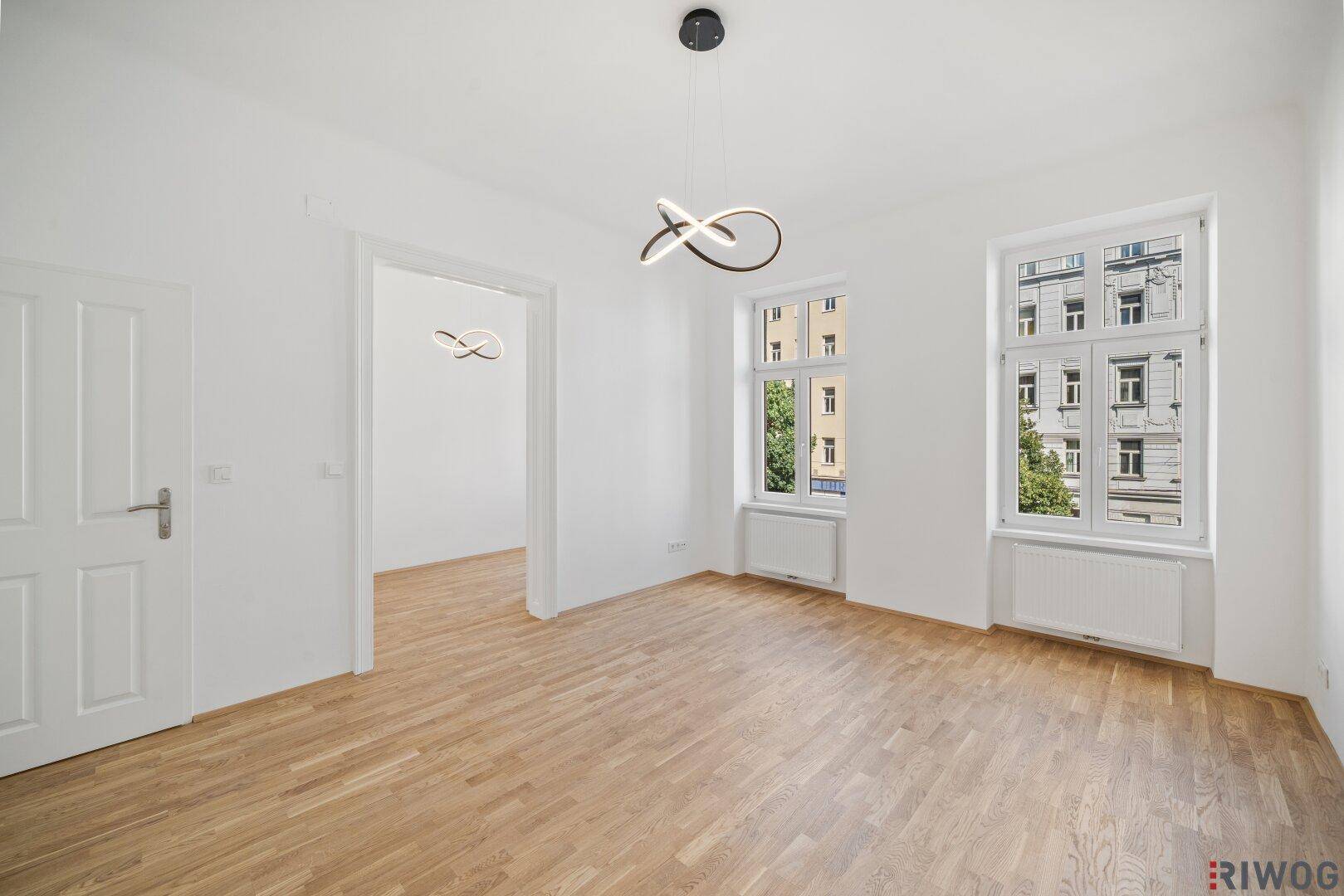 Geräumiges, helles Zimmer mit Parkettboden und Blick auf die umliegenden Gebäude.