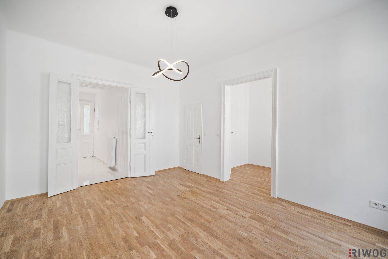 Heller Raum mit Parkettboden und mehreren Türen, die zu anderen Bereichen der Wohnung führen.