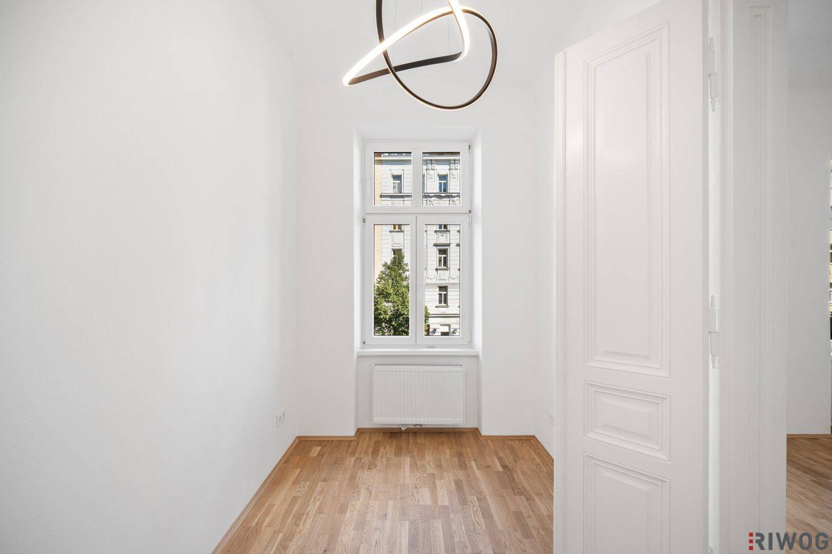 Kleineres, helles Zimmer mit Parkettboden und einem Fenster mit Blick ins Grüne.