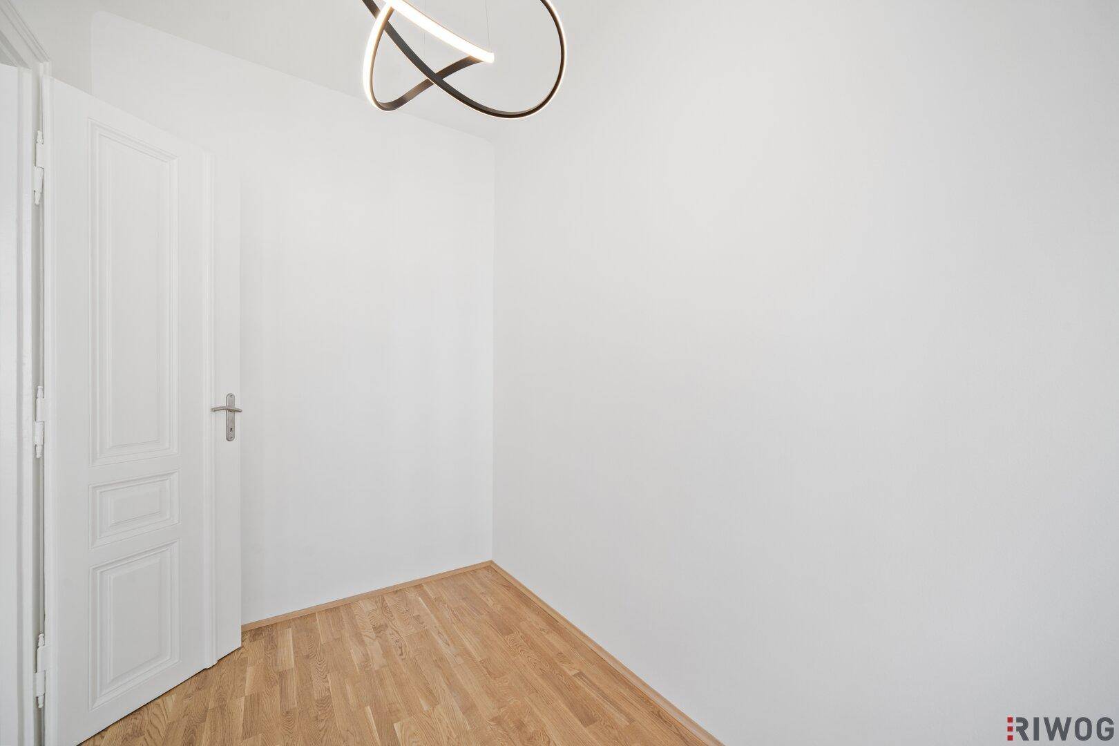 Leeres Zimmer mit Parkettboden und einer weißen Tür, bereit für individuelle Gestaltung.