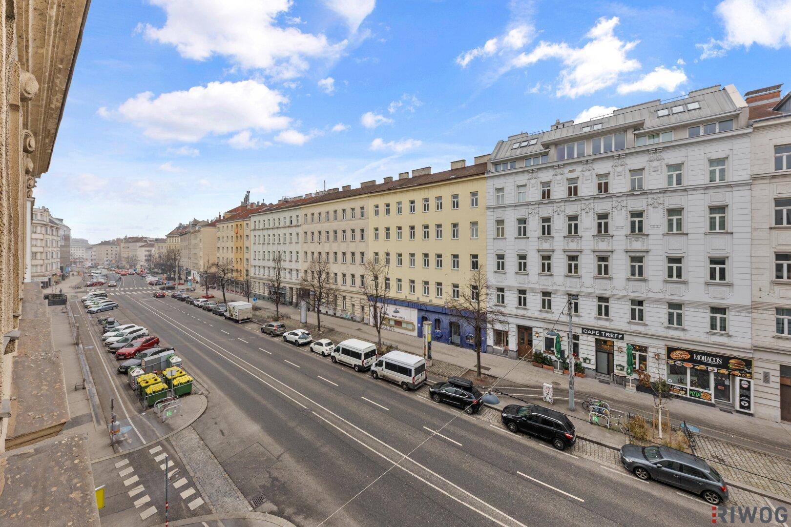 Weitläufiger Blick von einem Gebäude auf eine belebte Stadtstraße mit Gebäuden und Fahrzeugen.