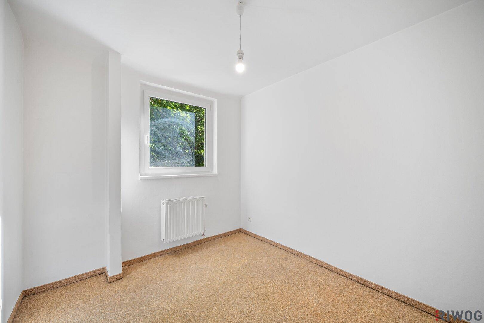 Helles Schlafzimmer mit Korkboden, weißen Wänden und Fenster mit Blick ins Grüne.