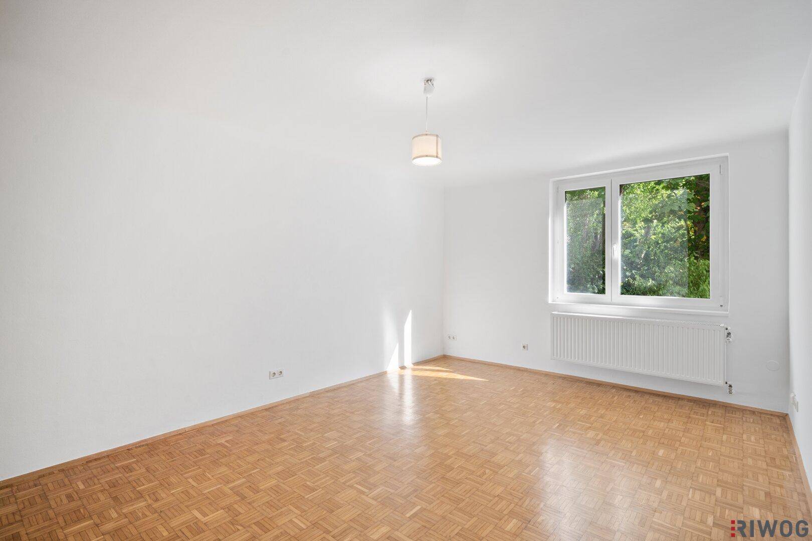 Lichtdurchflutetes Zimmer mit klassischem Parkettboden und Blick ins Grüne.