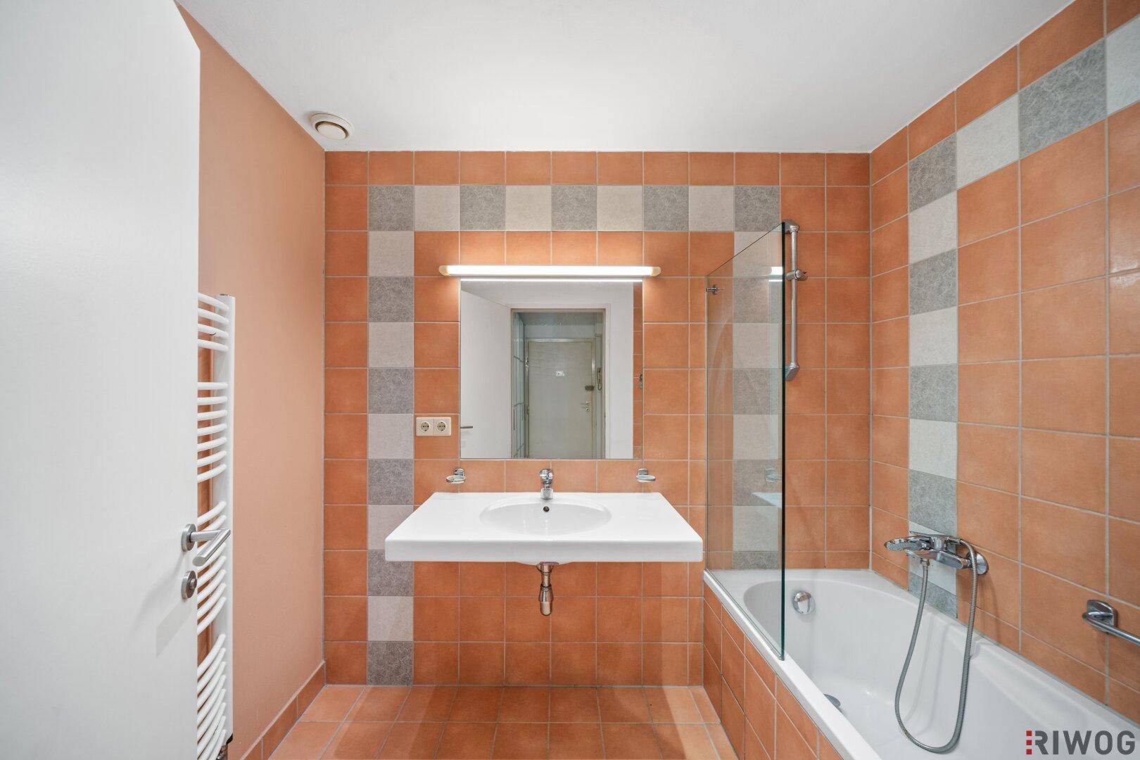 Badezimmer mit orangefarbenen Fliesen, Badewanne mit Duschwand und modernem Waschtisch.