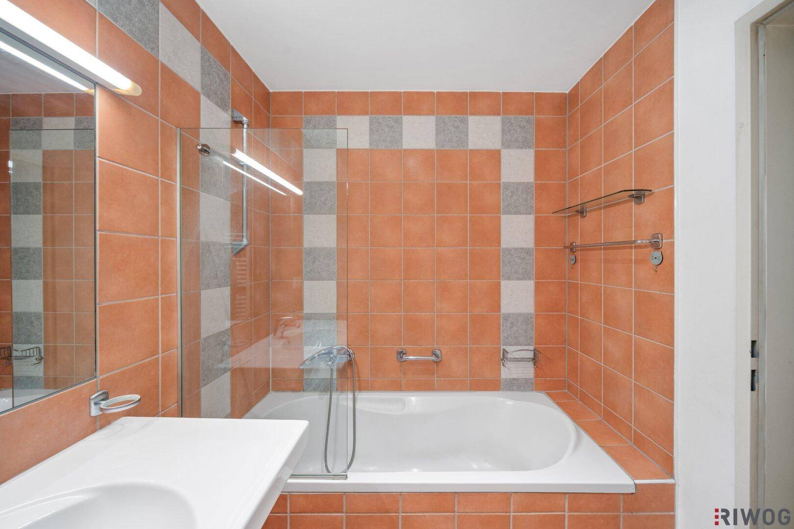 Gefliestes Badezimmer mit Badewanne, Duschabtrennung und Handtuchhalter.