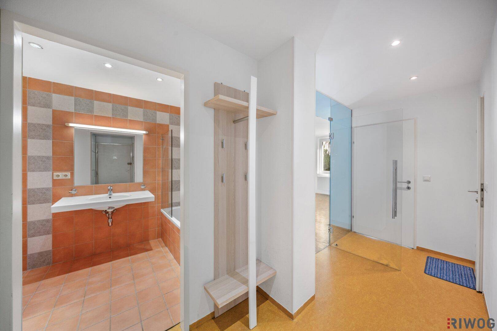 Heller Flur mit Garderobe, Zugang zum Badezimmer und Glaswand zum Wohnbereich.