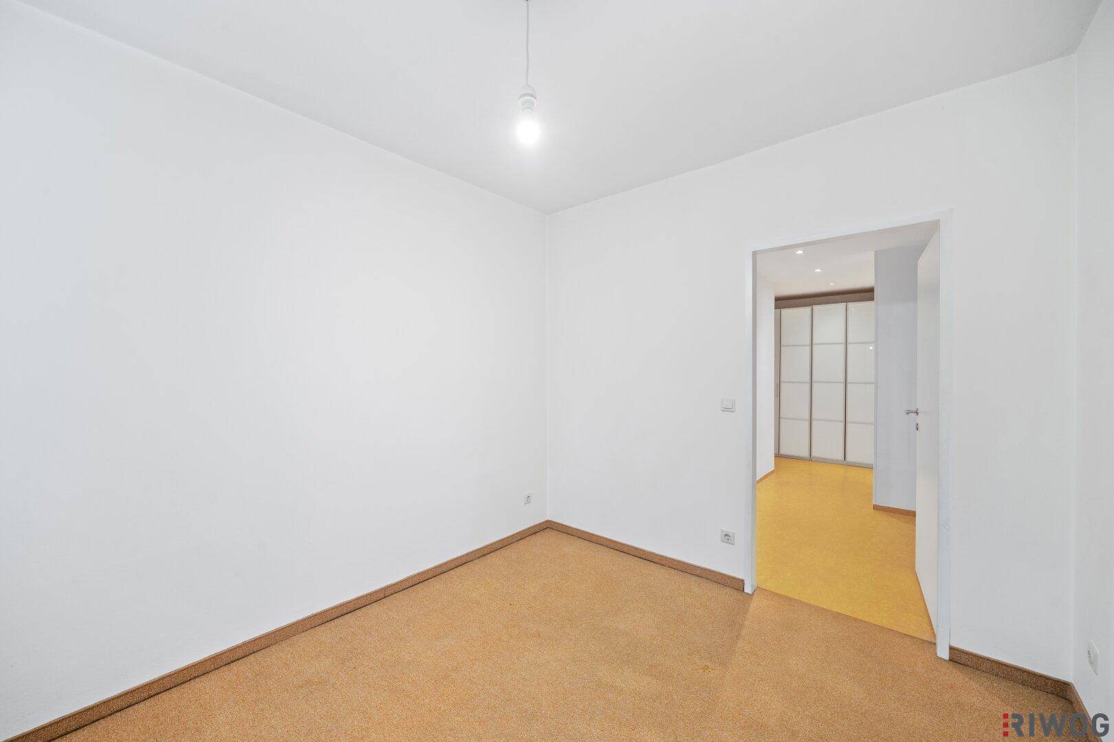 Zimmer mit Korkboden und Zugang zu einem Bereich mit praktischen Einbauschränken.
