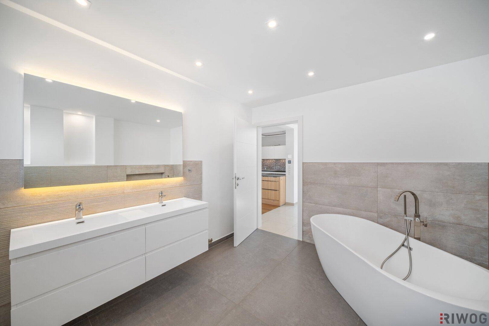 Modernes Badezimmer mit freistehender Badewanne, Doppelwaschbecken und großem beleuchtetem Spiegel.