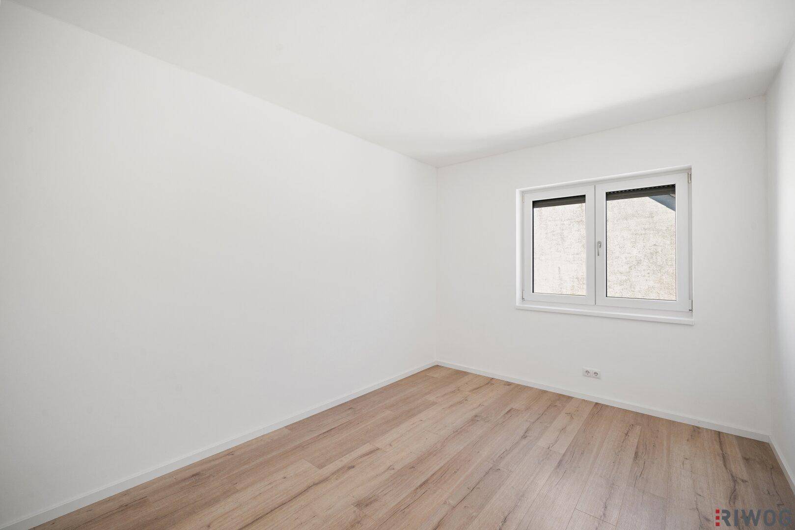 Neutral gestaltetes Zimmer mit Holzboden und Fenster, bereit zur individuellen Einrichtung.