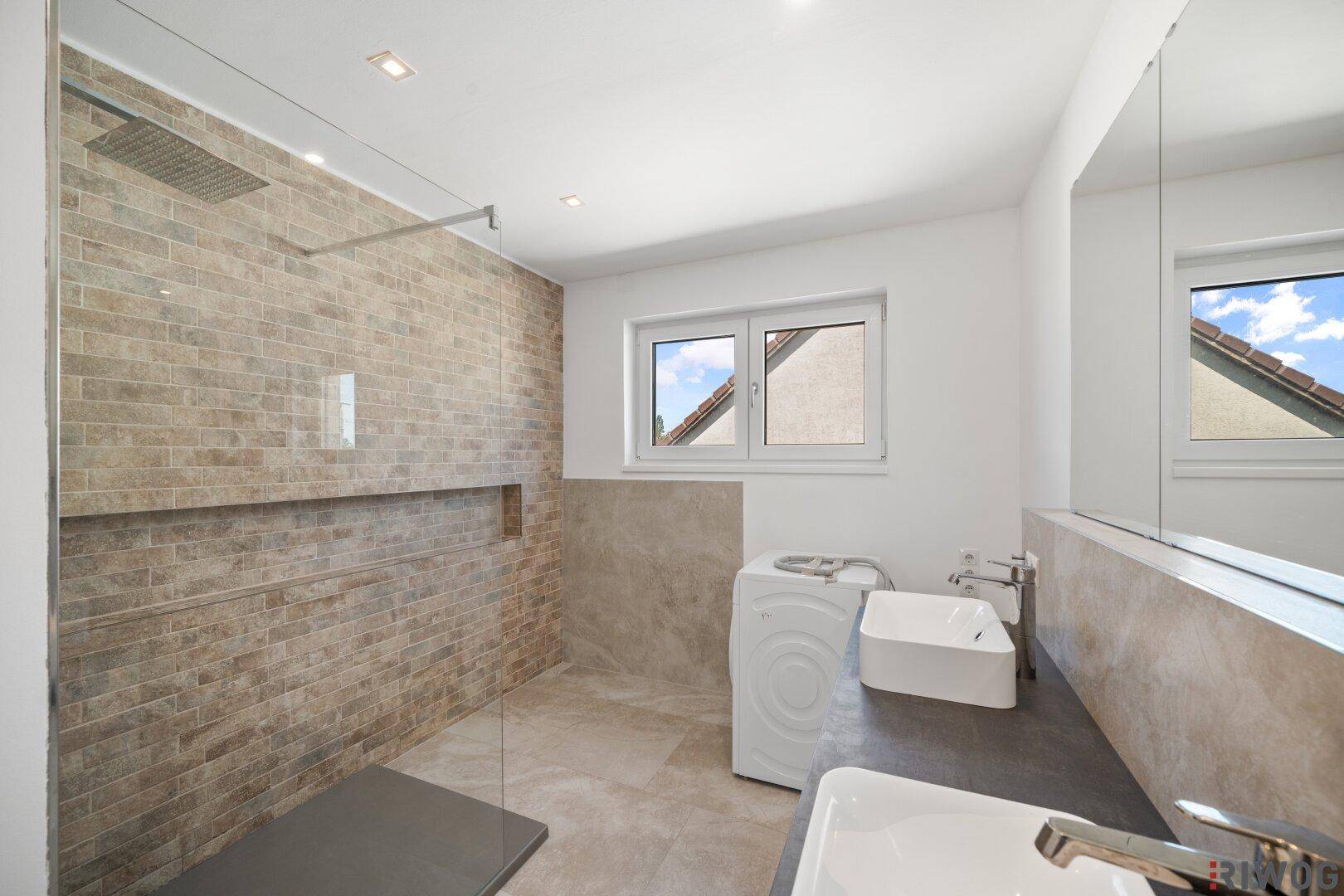 Modernes Badezimmer mit großer begehbarer Dusche, Doppelwaschbecken und Waschmaschine.