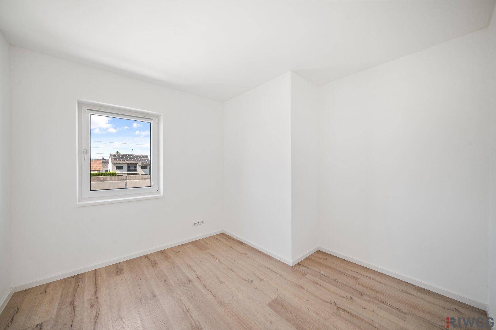 Helles Zimmer mit Holzboden und einem Fenster, das viel Tageslicht in den Raum bringt.
