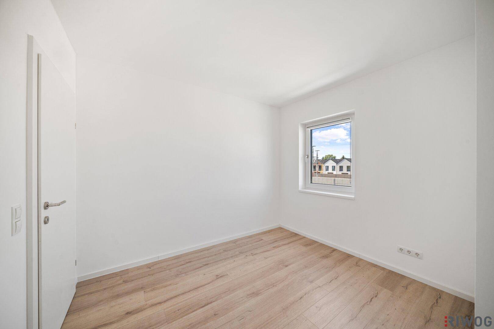 Neutral gestaltetes Zimmer mit Holzboden und Fenster, bereit für individuelle Gestaltung.